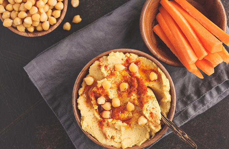 Hummus, fresh carrot sticks and boiled chickpeas in wooden bowls
