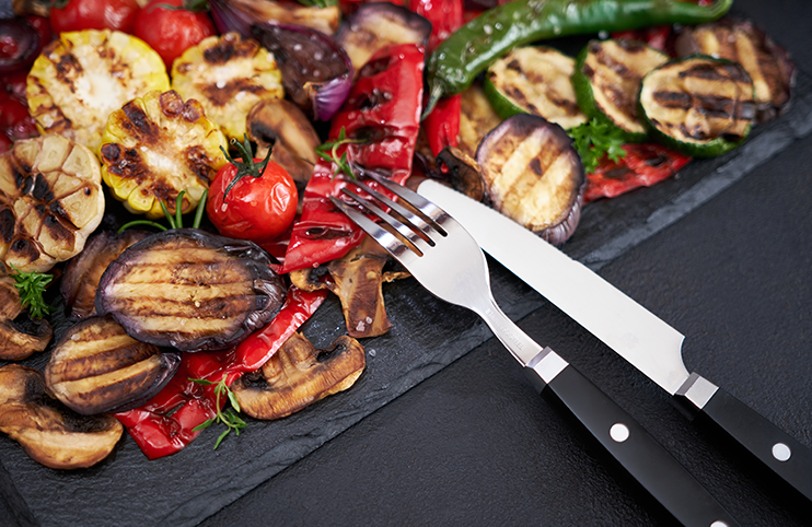 Grilled vegetables mix on a stone serving board - zucchini eggplant onions corn mushroom tomato