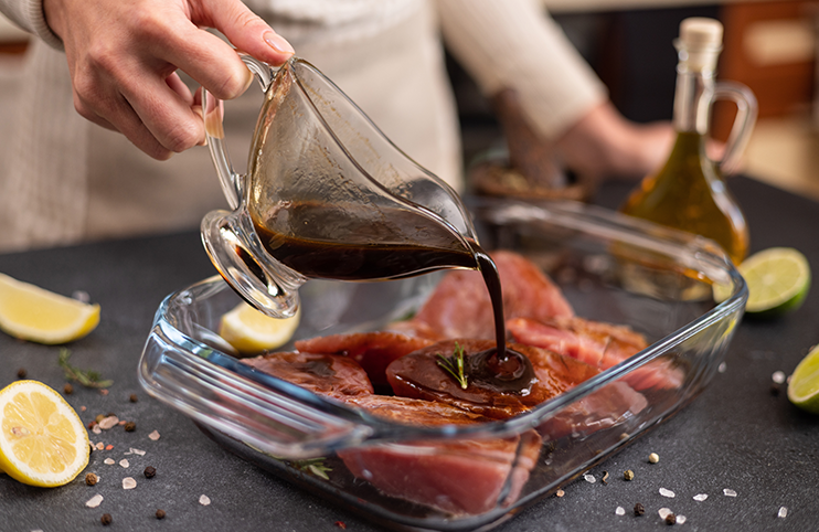 Woman pours soy sauce based marinade into glass cooking dish to marinate Pieces of Fresh tuna Fish fillet