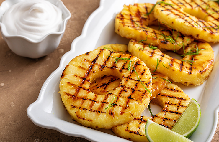 Grilled pineapple with lime honey glaze, lime zest and whipped cream on a serving plate